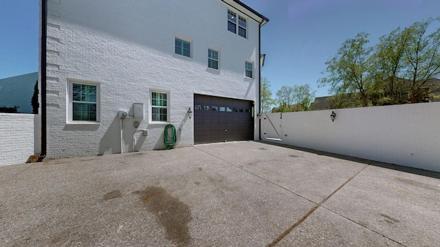 view of side of property featuring driveway, stone siding, a garage, and fence