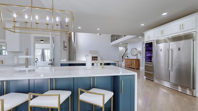 kitchen with recessed lighting, a kitchen bar, light wood-type flooring, stainless steel built in refrigerator, and white cabinets