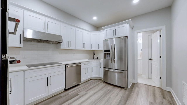 kitchen with stainless steel appliances, under cabinet range hood, light wood-type flooring, backsplash, and light countertops