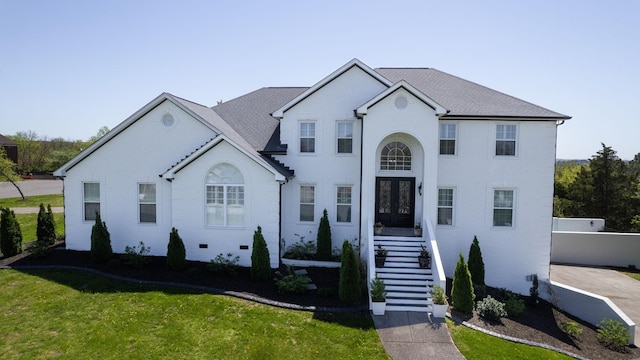 view of front of property featuring brick siding, french doors, stairway, and a front yard