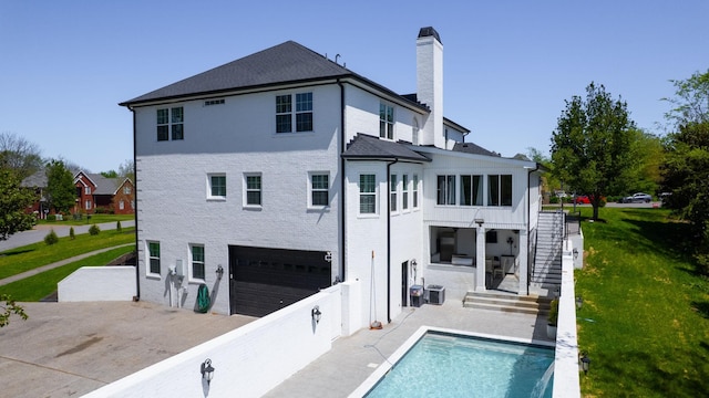 back of house featuring stairway, a yard, an outdoor pool, a chimney, and an attached garage