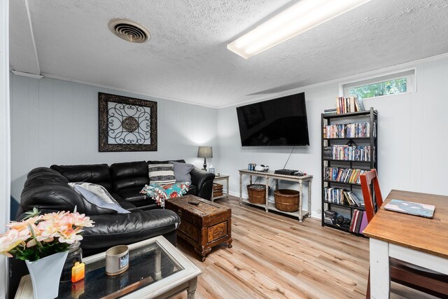 living room with ornamental molding, a textured ceiling, visible vents, and wood finished floors
