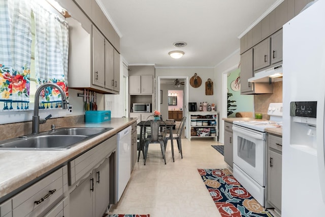 kitchen featuring white appliances, under cabinet range hood, crown molding, and a sink