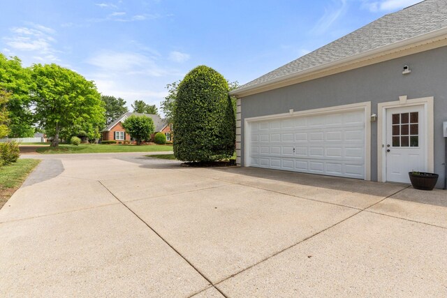 view of property exterior featuring a shingled roof, stucco siding, and concrete driveway