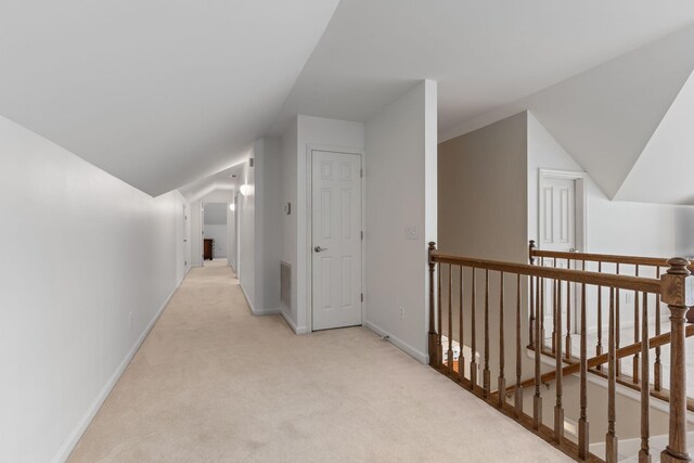 corridor featuring light colored carpet, baseboards, an upstairs landing, lofted ceiling, and visible vents