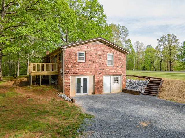 view of property exterior featuring french doors, a chimney, a wooden deck, brick siding, and gravel driveway