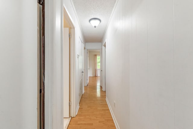 hall with baseboards, light wood-type flooring, and a textured ceiling