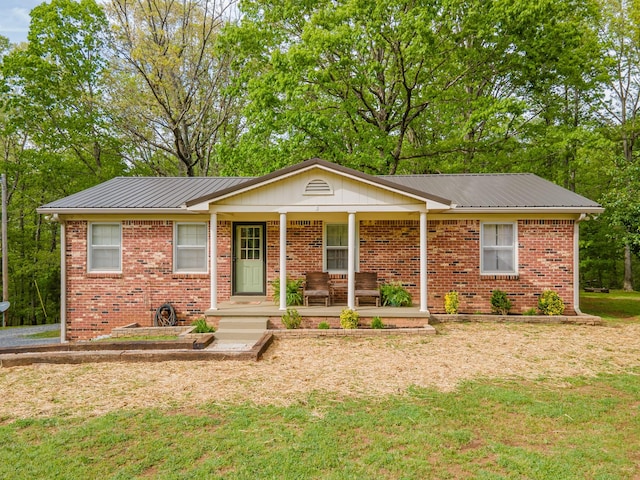 ranch-style house featuring metal roof, a porch, a front lawn, and brick siding