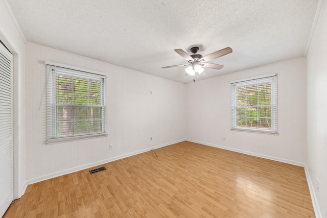 unfurnished bedroom with a textured ceiling, multiple windows, light wood-style flooring, and visible vents