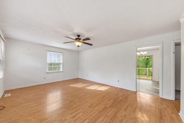 spare room with visible vents, plenty of natural light, light wood-style flooring, and ceiling fan with notable chandelier