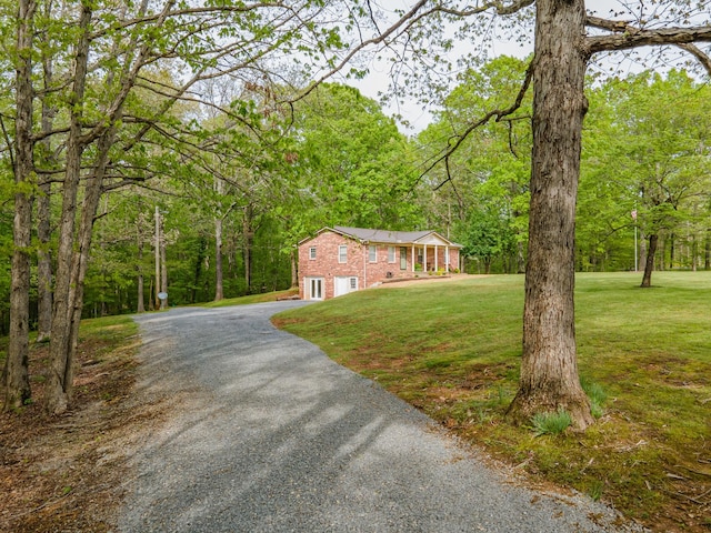 view of front of house featuring an attached garage, a view of trees, driveway, and a front yard
