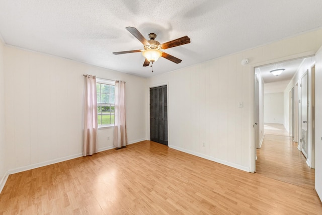 empty room featuring a ceiling fan, baseboards, light wood finished floors, and a textured ceiling