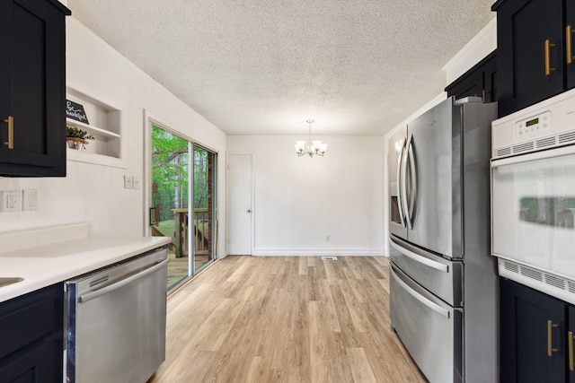 kitchen featuring light wood-style floors, a textured ceiling, appliances with stainless steel finishes, light countertops, and an inviting chandelier