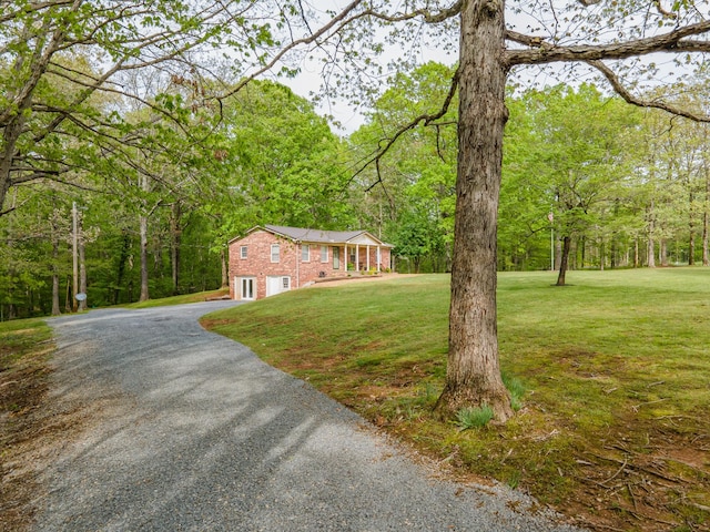view of front of house featuring a front lawn, brick siding, a garage, gravel driveway, and a wooded view