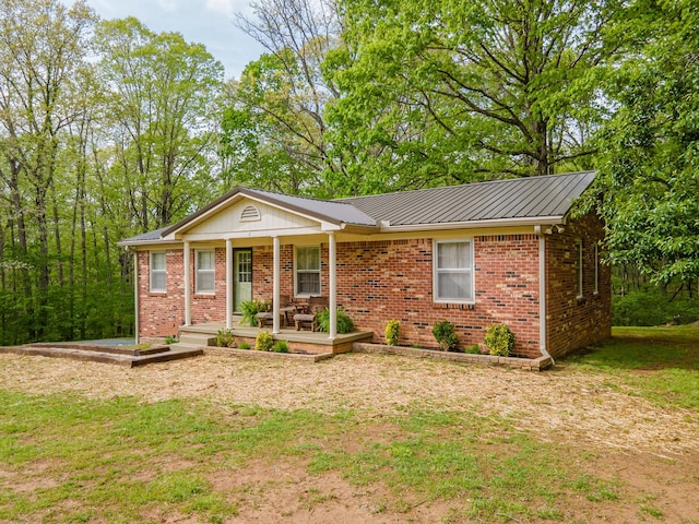 single story home featuring covered porch, brick siding, metal roof, and a front yard
