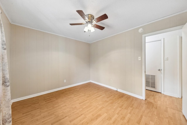 empty room with visible vents, ornamental molding, light wood-style floors, baseboards, and ceiling fan