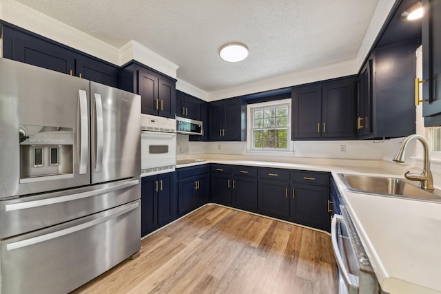 kitchen featuring stainless steel appliances, a textured ceiling, a sink, and light wood-type flooring