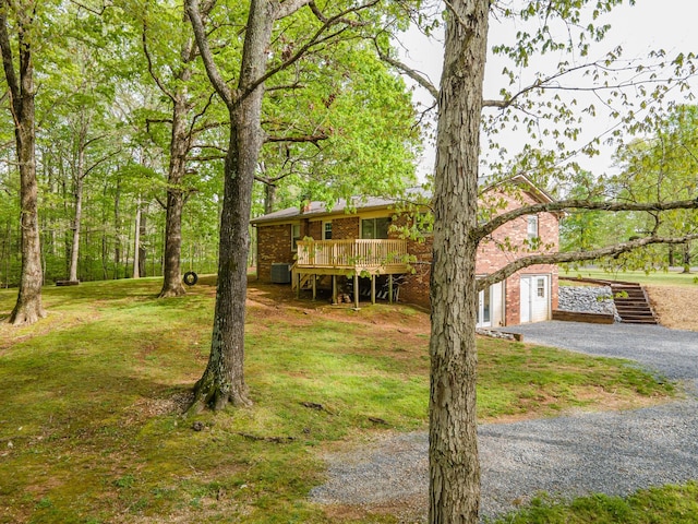 view of front facade featuring brick siding, stairway, a deck, a front yard, and gravel driveway