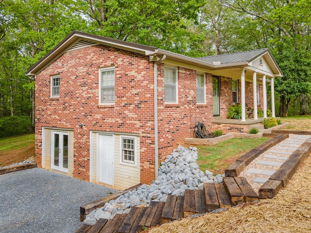 view of property exterior with french doors, a porch, and brick siding