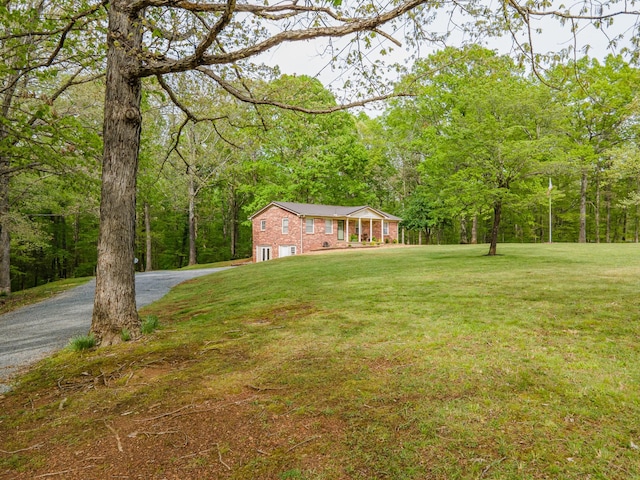 view of yard featuring a garage, a view of trees, and gravel driveway