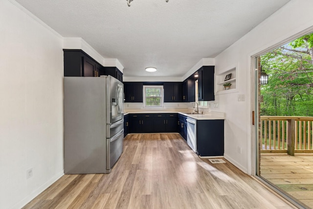kitchen featuring a sink, light countertops, dark cabinets, light wood-style flooring, and stainless steel appliances