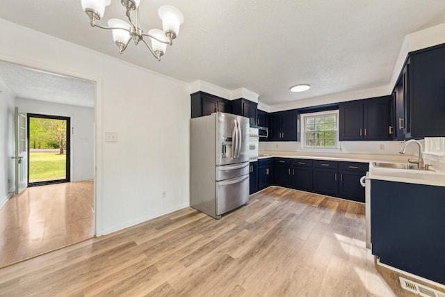 kitchen featuring a sink, light countertops, light wood finished floors, a chandelier, and stainless steel appliances