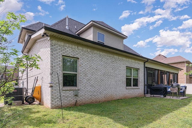 rear view of property featuring a lawn, central AC unit, a patio area, a sunroom, and brick siding