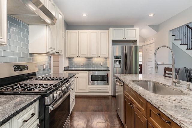 kitchen featuring dark stone countertops, ventilation hood, a sink, dark wood finished floors, and appliances with stainless steel finishes