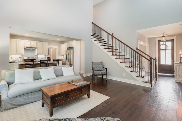 living area featuring a high ceiling, recessed lighting, baseboards, wood finished floors, and stairway