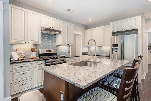 kitchen with dark wood-type flooring, under cabinet range hood, a sink, dark stone countertops, and appliances with stainless steel finishes