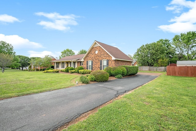 view of front of home featuring driveway, brick siding, fence, a front lawn, and a shingled roof