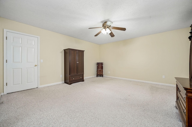 interior space with light colored carpet, a ceiling fan, baseboards, and a textured ceiling
