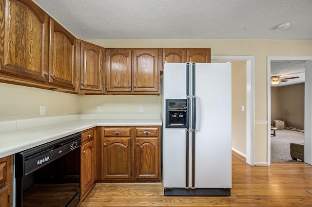 kitchen with brown cabinetry, black dishwasher, white refrigerator with ice dispenser, a textured ceiling, and light wood-style flooring