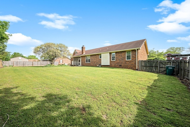 back of house featuring a fenced backyard, a chimney, a lawn, and brick siding