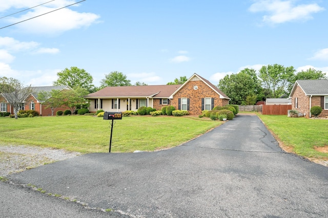 ranch-style home featuring brick siding, aphalt driveway, fence, and a front lawn