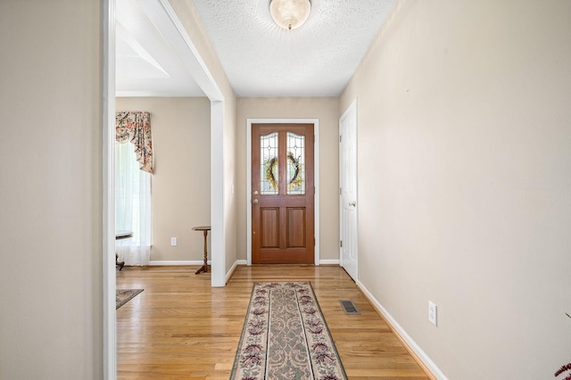 foyer entrance with visible vents, a textured ceiling, light wood-style floors, and baseboards