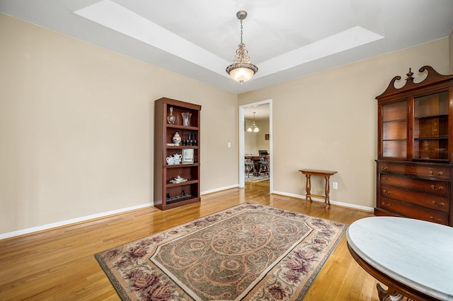 living area with baseboards, a raised ceiling, wood finished floors, and a skylight