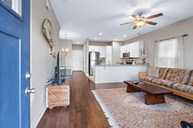 living room featuring dark wood-style flooring, baseboards, recessed lighting, and ceiling fan with notable chandelier