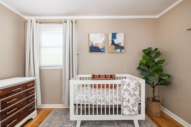 bedroom with baseboards, ornamental molding, light wood finished floors, and a nursery area