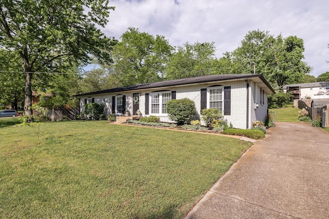 ranch-style house featuring brick siding, a front lawn, fence, and driveway