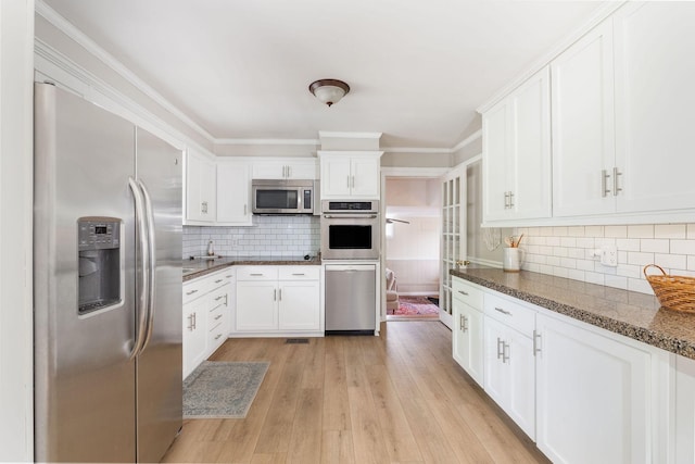kitchen with light wood-style floors, appliances with stainless steel finishes, tasteful backsplash, and white cabinetry