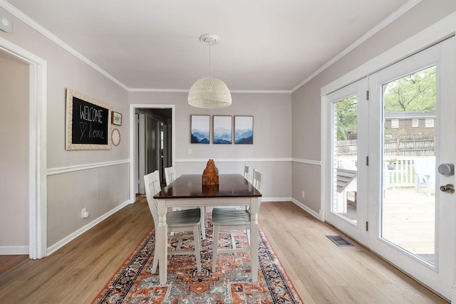 dining room with light wood-style floors, baseboards, crown molding, and visible vents