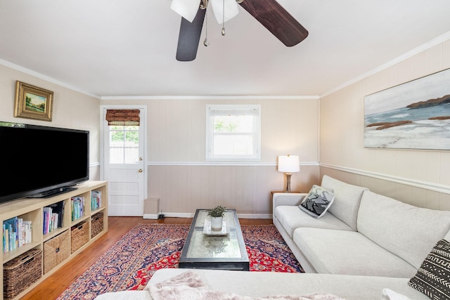 living room with crown molding, a ceiling fan, wood walls, and wood finished floors