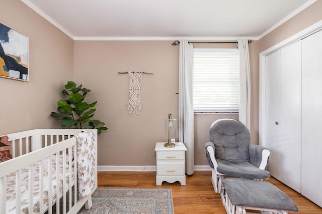 bedroom with crown molding, a nursery area, baseboards, light wood-type flooring, and a closet