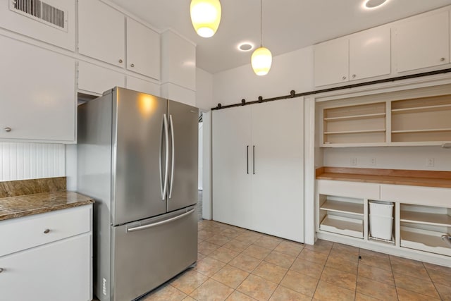kitchen featuring visible vents, freestanding refrigerator, a barn door, white cabinets, and light tile patterned floors