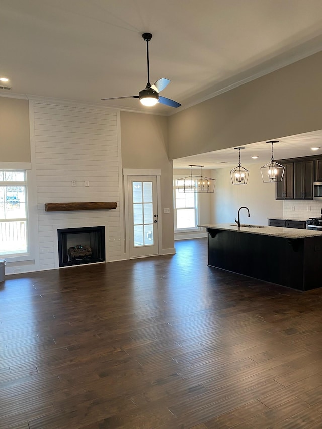 unfurnished living room with crown molding, a large fireplace, a sink, and ceiling fan with notable chandelier