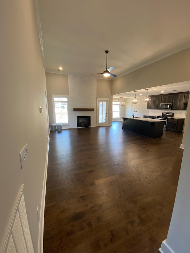unfurnished living room featuring ornamental molding, dark wood-style flooring, baseboards, ceiling fan, and a large fireplace