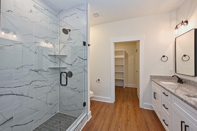 full bath with visible vents, double vanity, wood finished floors, a sink, and a marble finish shower