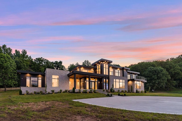 view of front of house with fence, a front lawn, stone siding, a balcony, and a patio