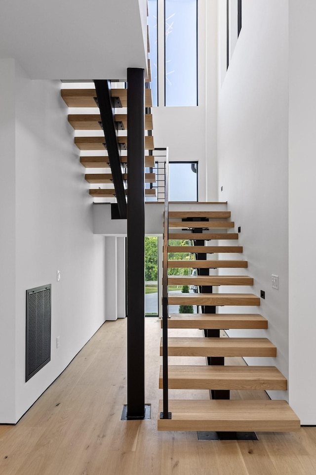 stairway featuring plenty of natural light, visible vents, wood finished floors, and a towering ceiling
